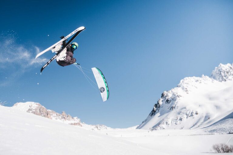 Schifahrer springt mit Kite im Schnee