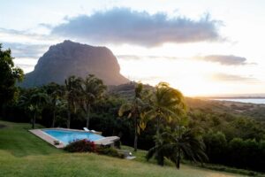 Blick von der Unterkunft in Mauritius über grüne Wiesen mit einem Pool in einem Palmenhain auf den Brabant und die Bucht mit flachem Wasser