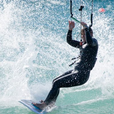 Frau auf Waveboard beim Female Kitecamp in Portugal in der Welle mit viel Spray