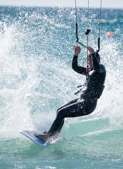 Frau auf Waveboard beim Female Kitecamp in Portugal in der Welle mit viel Spray